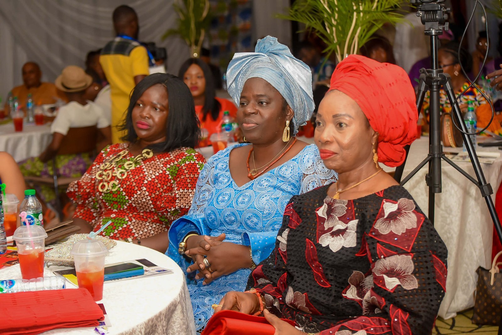 Three women in geles and African prints seated at a reception table